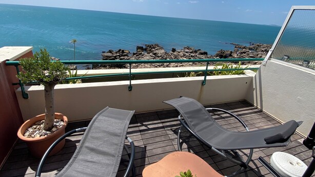 A balcony with two lounge chairs, a small table, and a potted plant. The balcony overlooks a rocky shoreline and the ocean. - Modern apartment breathtaking sea view and waterfront (Sète)