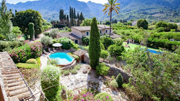 En villa med swimmingpool, omgivet af frodig vegetation og bjerge i baggrunden.