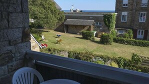 A balcony with a view of a grassy yard, a stone wall, and a building with a chimney. - Flat with seaview - 50m from beach- 3/4 persons (Carnac)