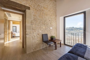 A room with a stone wall, a balcony with a view, a wooden floor, and a bed.