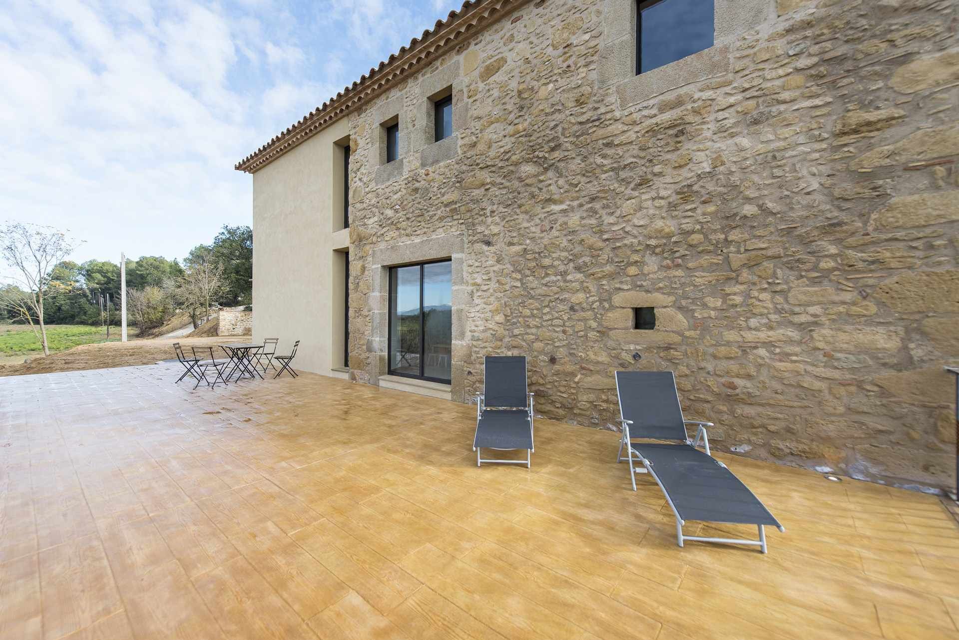 A stone building with a patio, two lounge chairs, and a table with chairs.