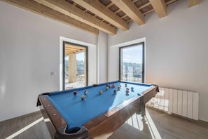 A pool table with balls, a wooden ceiling, and large windows.
