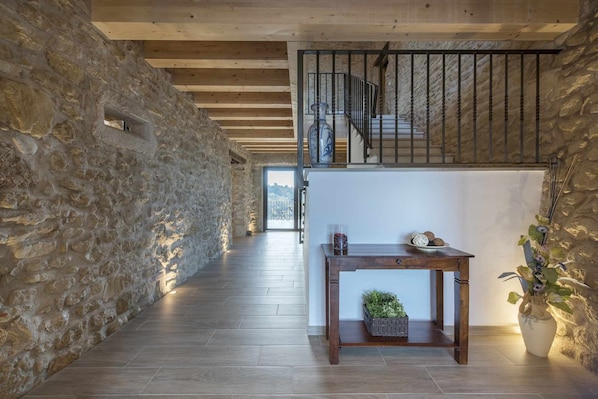 A stone-walled hallway with wooden flooring, a staircase, and a table with a vase and decorative items.