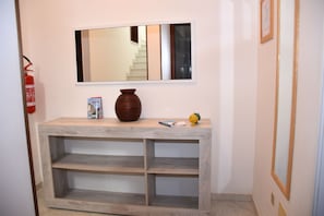 A hallway with a wooden console table, a vase, a framed mirror, and a fire extinguisher.