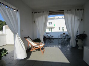 Une terrasse ensoleillée avec une chaise en bois, une petite table et une plante en pot.