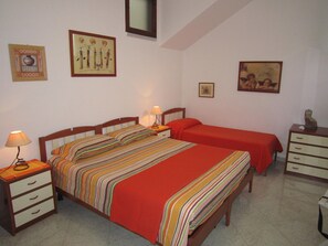 Une chambre avec un grand lit, deux tables de chevet, une commode et un meuble à tiroirs. Les murs sont ornés de tableaux et il y a un miroir.