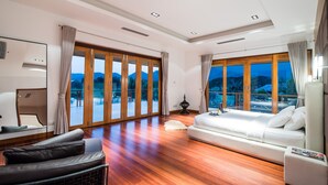 A spacious room with a large bed, a sofa, and a chair. There are large windows with curtains, a ceiling fan, and a wall-mounted TV. - Golf Resort /Villa in Hua Hin, Palm Hills Golf Resort (Tambon Hua Hin)