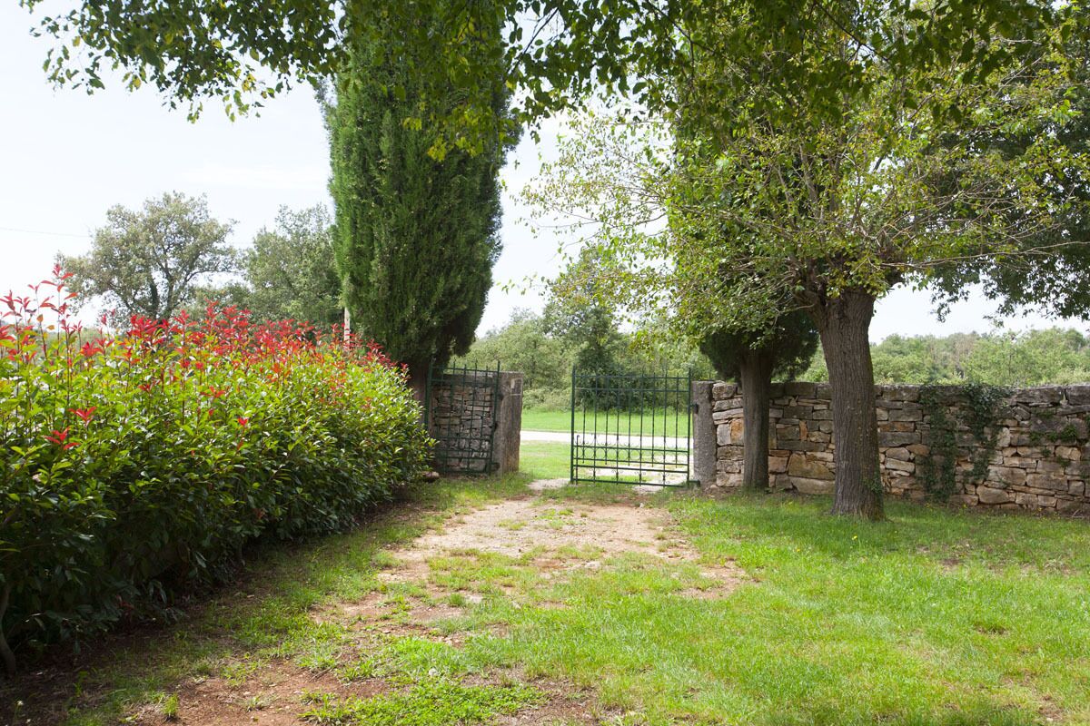 A pathway leading to a gated entrance surrounded by lush greenery and a stone wall.