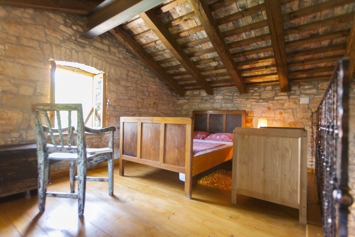Ein rustikaler Raum mit einem Holzbett, einem Stuhl und einer Steinwand.