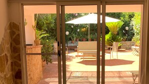 A room with a sliding glass door leading to an outdoor patio area with a table, chairs, and potted plants. - Greek/Mediterranean style villa of 200 sqm, with elegant interiors, family friendly (Pilone)