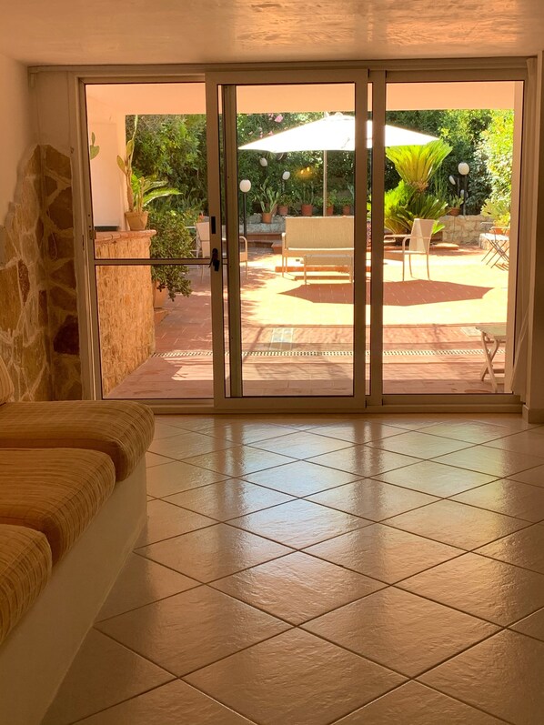 A room with a sliding glass door leading to an outdoor patio area with a table, chairs, and potted plants.