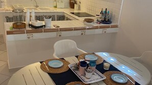 A dining area with a round table set for four, white chairs, and a kitchen in the background. - Greek/Mediterranean style villa of 200 sqm, with elegant interiors, family friendly (Pilone)