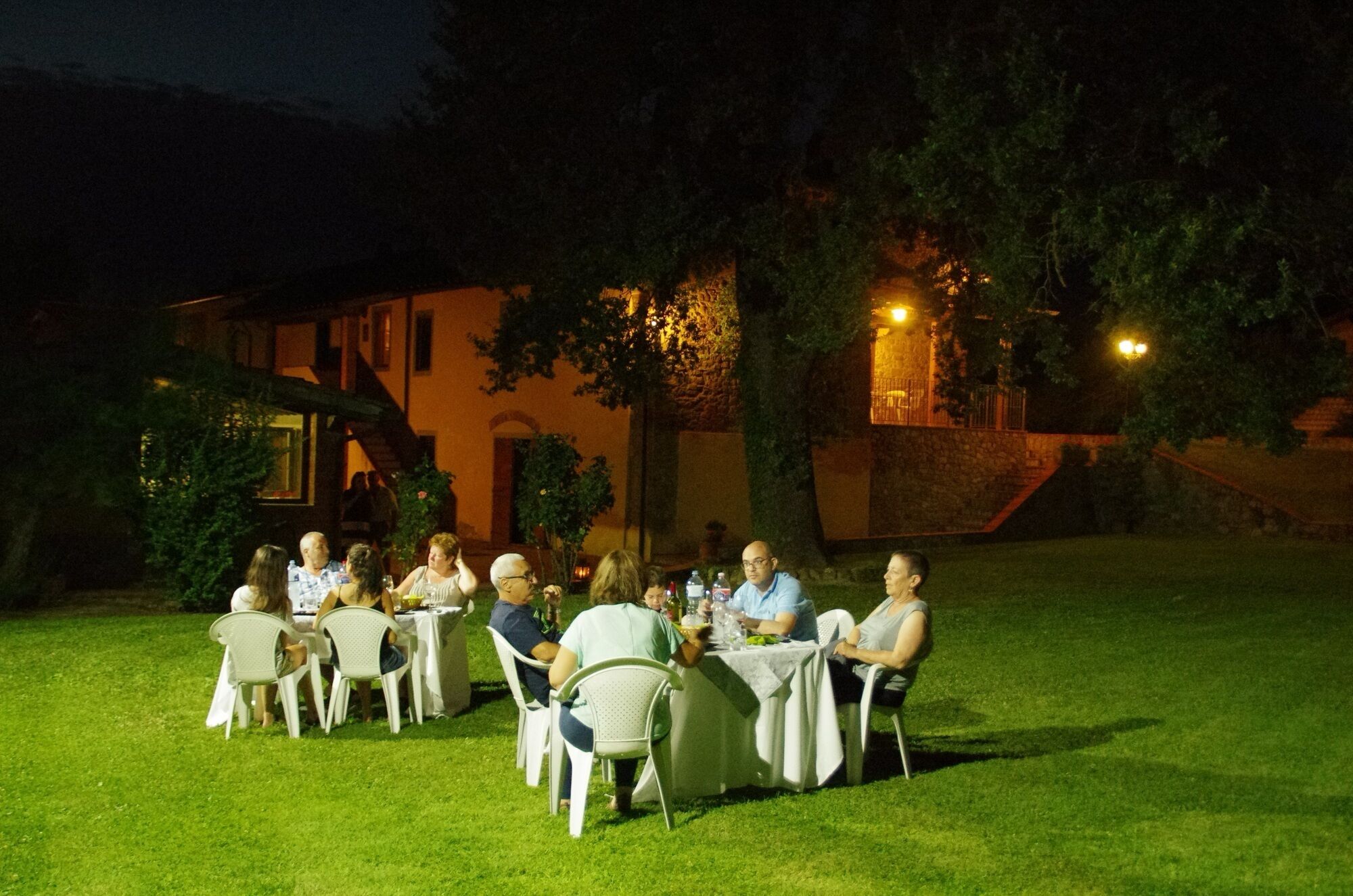 An outdoor dining area with tables and chairs, surrounded by a grassy lawn and trees.