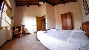 A bedroom with a large bed, wooden wardrobe, and a desk with a chair.