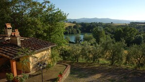 A rustic house with a tiled roof, a garden with potted plants, and a view of a lake and mountains in the distance.