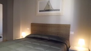 Un lit bien fait, avec une tête de lit, deux lampes de chevet et un tableau représentant un voilier accroché au mur.