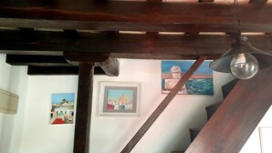 Techo de madera con una lámpara colgante, una escalera y dos cuadros enmarcados en la pared.