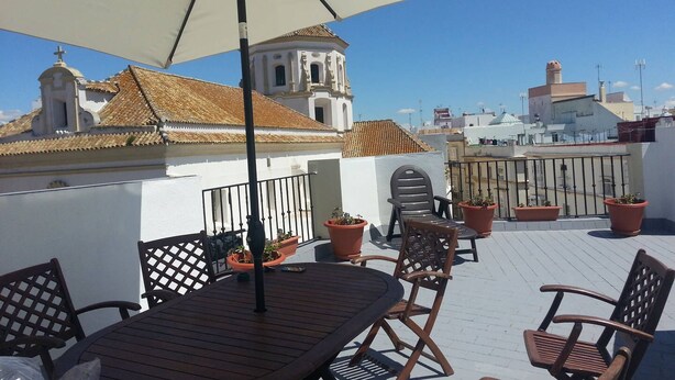 Una terraza en la azotea con una mesa y sillas, plantas en macetas y vistas a una iglesia con un campanario.