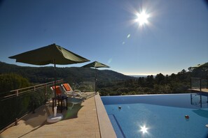 A rooftop infinity pool with a clear view of the surrounding landscape, including hills and trees.
