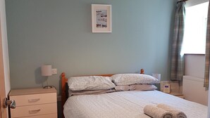 Ein Schlafzimmer mit einem Bett, einem Nachttisch, einer Lampe, einer Kommode und einem gerahmten Bild an der Wand.