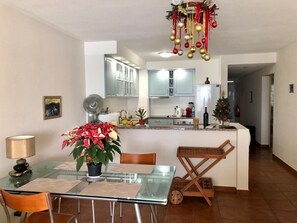 Eine moderne Küche mit weißen Schränken, einer zentralen Kochinsel und einem Essbereich mit einem Glastisch und Stühlen.