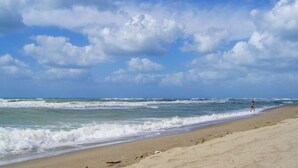 Una playa con olas y una persona caminando.