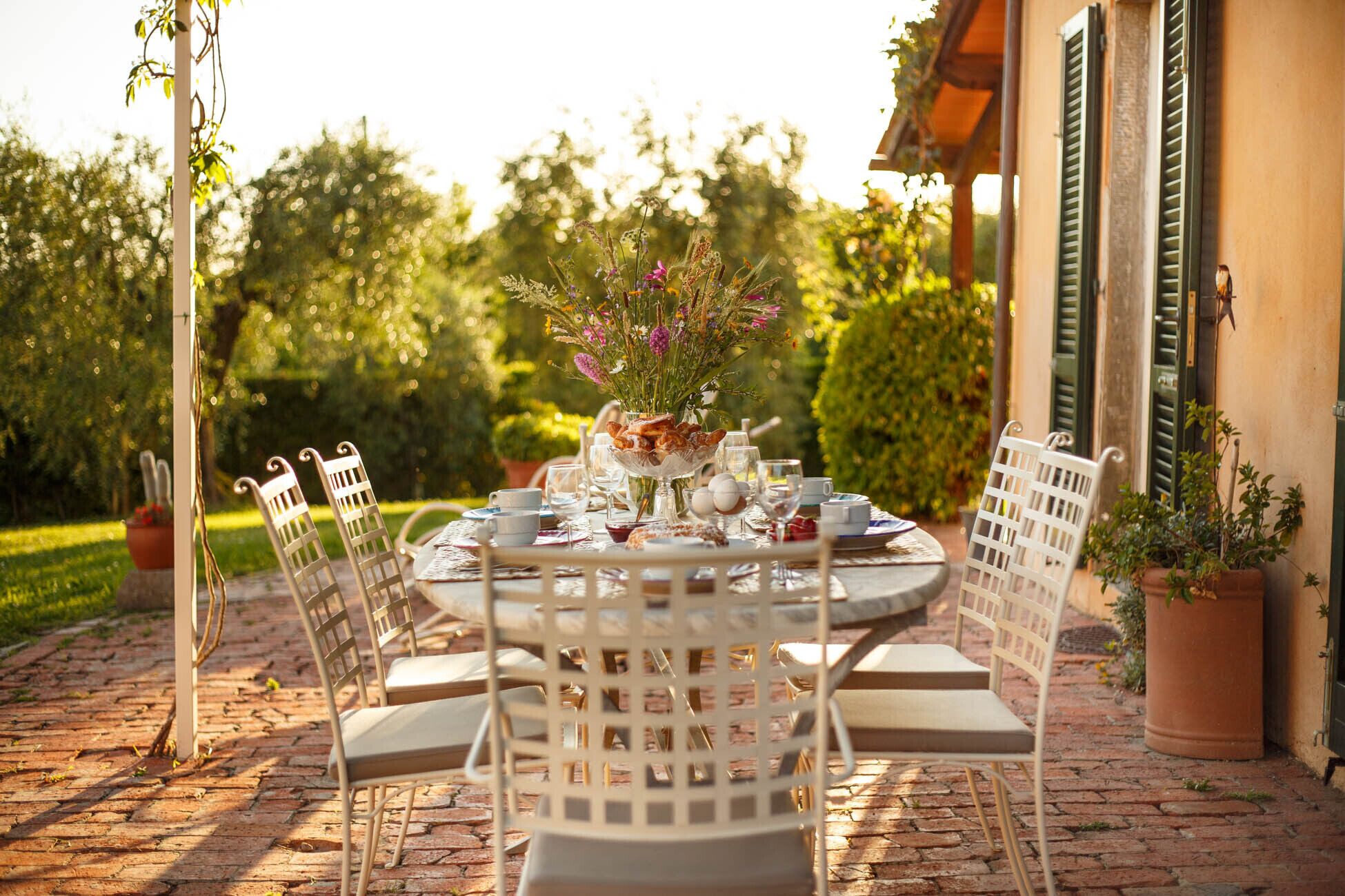 An outdoor dining area with a round table set for four, surrounded by white chairs with cushioned seats.