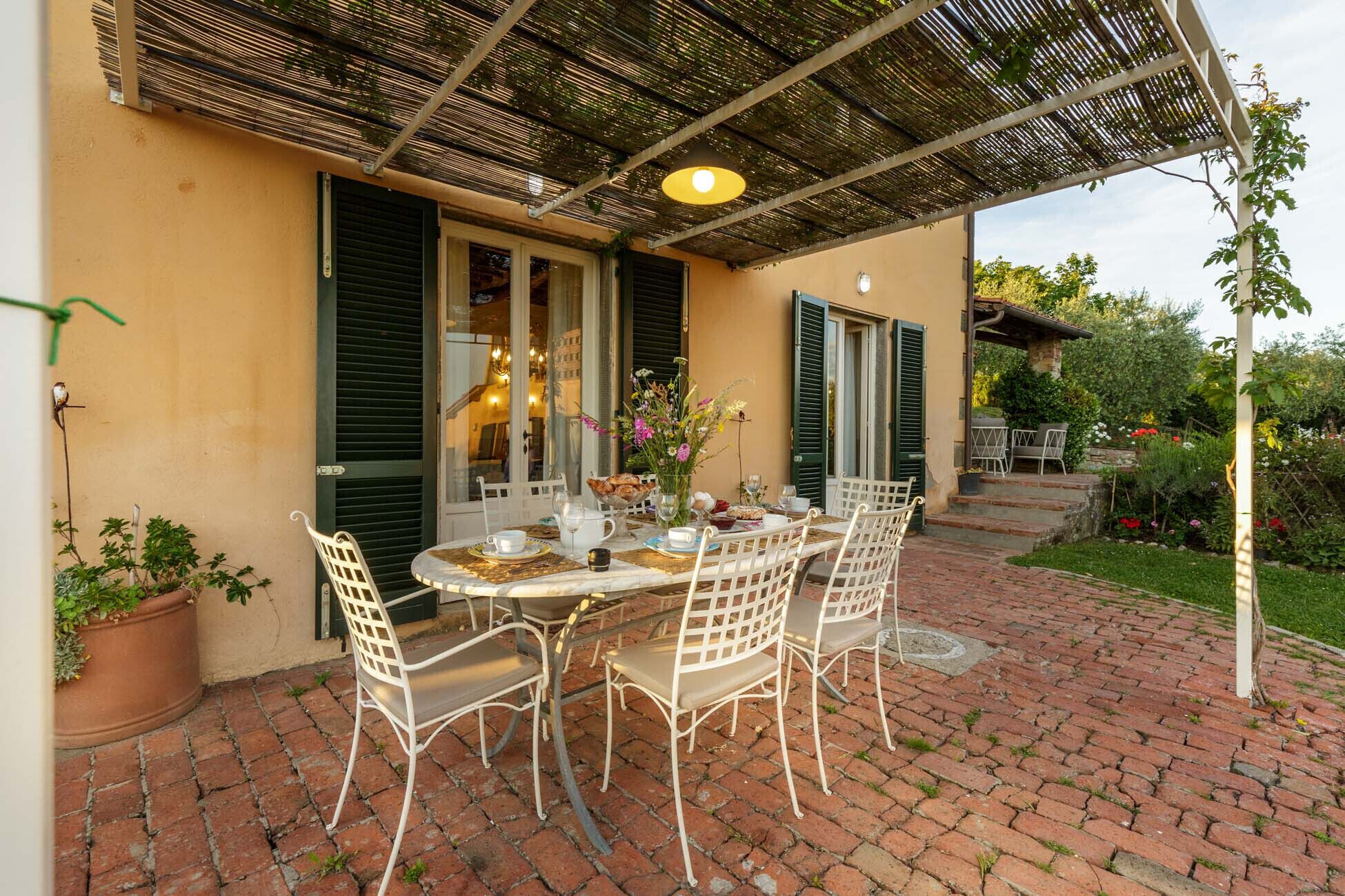 A patio with a round table set for four, surrounded by white chairs, under a pergola.