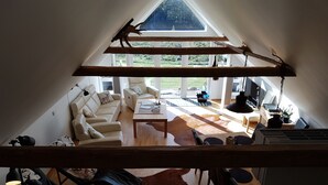 Un salón amplio con techo alto, una viga de madera, un conjunto de sofás, una mesa de centro y una mesa de comedor con sillas.