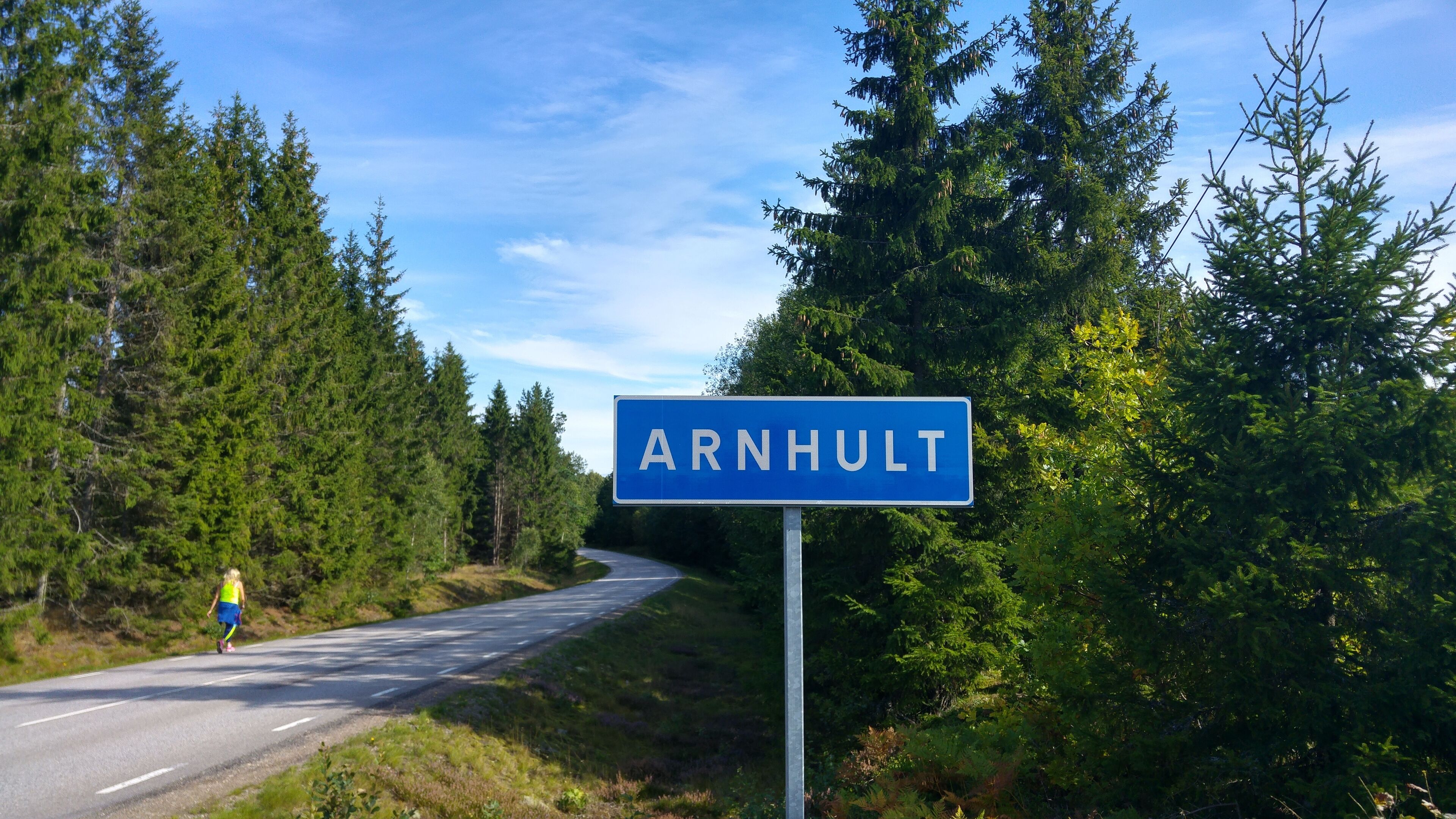 A road sign for ARNHULT with a runner in the background.