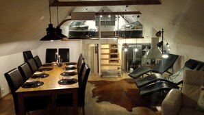 Un comedor con mesa de madera y sillas negras, un tapete de cuero de vaca, y un entrepiso con dormitorio arriba.