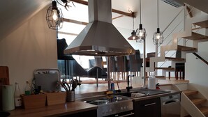 Una cocina moderna con una isla central, horno empotrado y electrodomésticos de acero inoxidable. Se observa una escalera que conduce a un nivel superior.