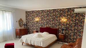 A bedroom with a floral wallpaper, a wooden bed frame, a red upholstered bench, and a brown leather sofa. - MAS with swimming pool 5 minutes from Saint Remy de Provence (Tarascon)