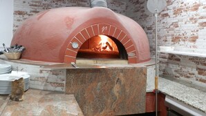 Tiilivuorattu pizzauuni, jossa on ajastin ja seinällä oleva kello.