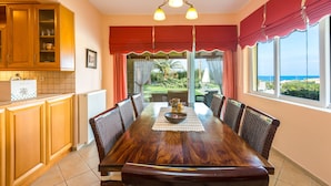 A dining area with a wooden table, chairs, a bowl, and a pitcher. There is a window with curtains and a view of the outdoors. - Malena Villa with Private Pool | Walking distance to beach & restaurants (Rethymno)