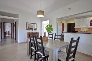 A modern kitchen with white cabinets, a wooden dining table, and a large plant. - Delightful single-storey villa, private pool, free air conditioning and wifi (Vilamoura)