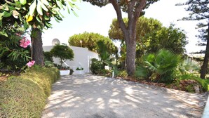 A paved pathway leading to a white building with a satellite dish, surrounded by lush greenery and trees. - Delightful single-storey villa, private pool, free air conditioning and wifi (Vilamoura)