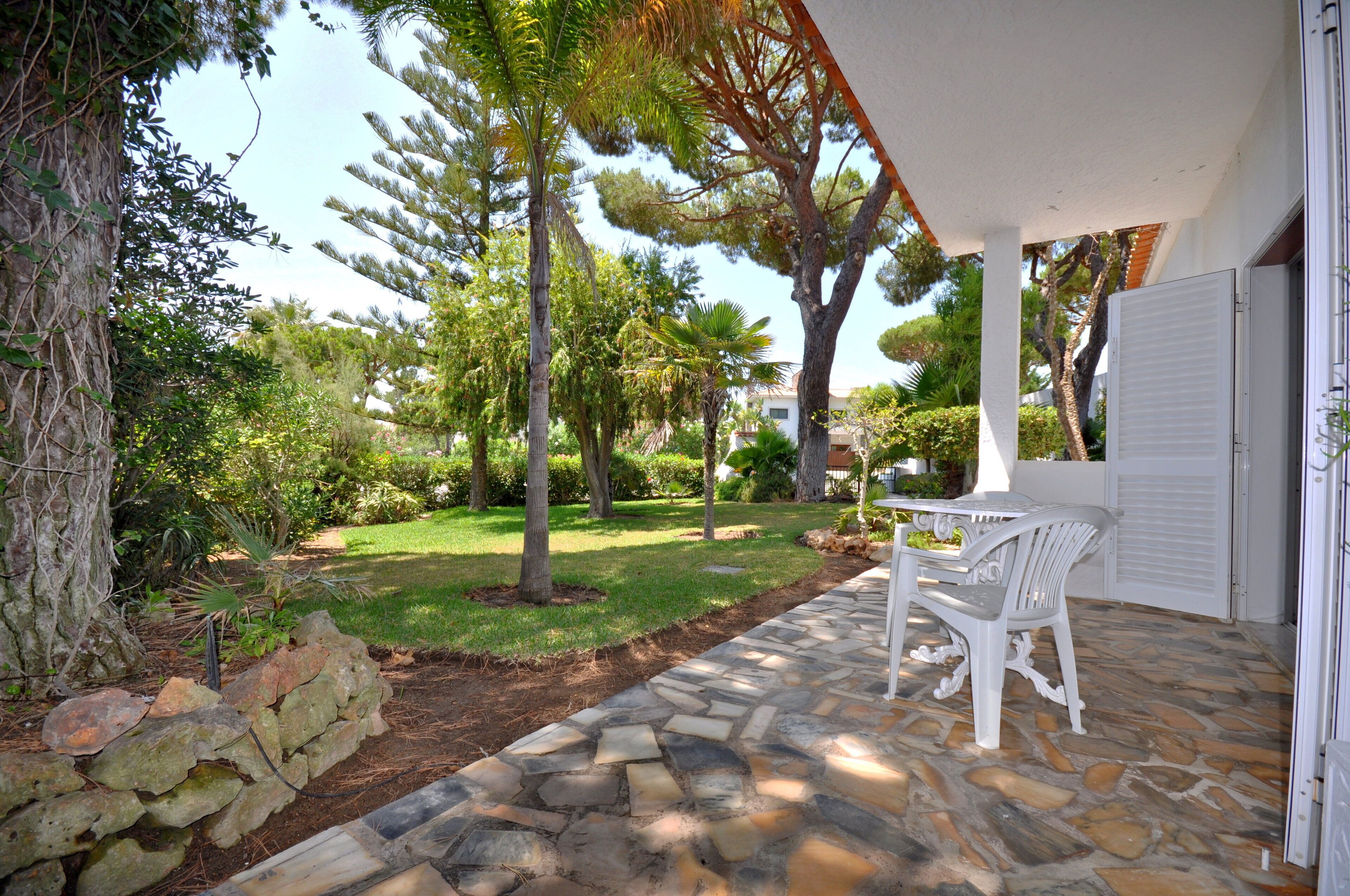 A patio with stone flooring, white chairs, and a table.