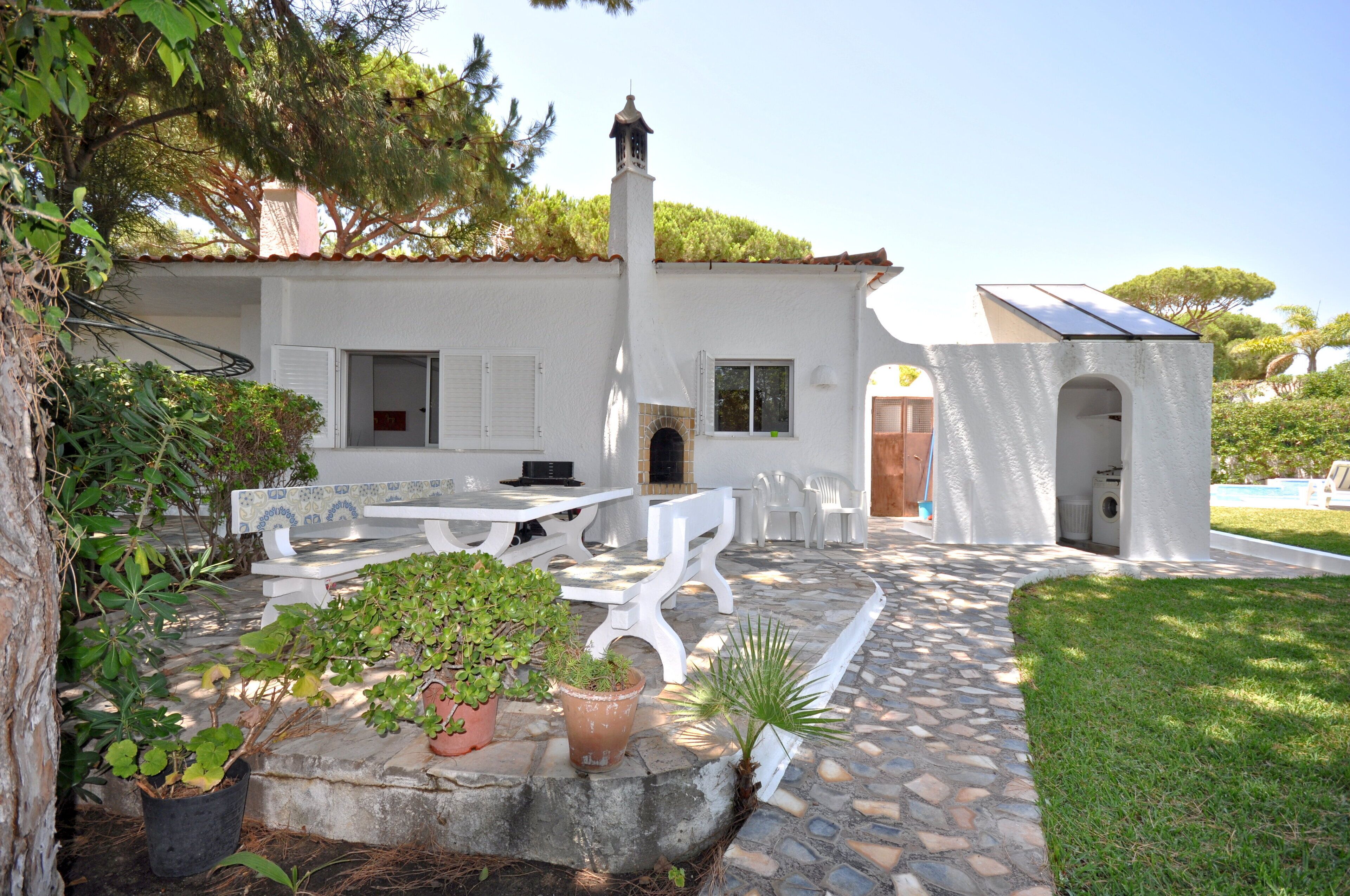 Un edificio blanco con un patio, mesas al aire libre y un pequeño jardín.