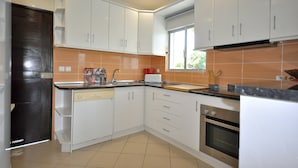 A modern kitchen with white cabinets, a built-in oven, and a window providing natural light. - Delightful single-storey villa, private pool, free air conditioning and wifi (Vilamoura)