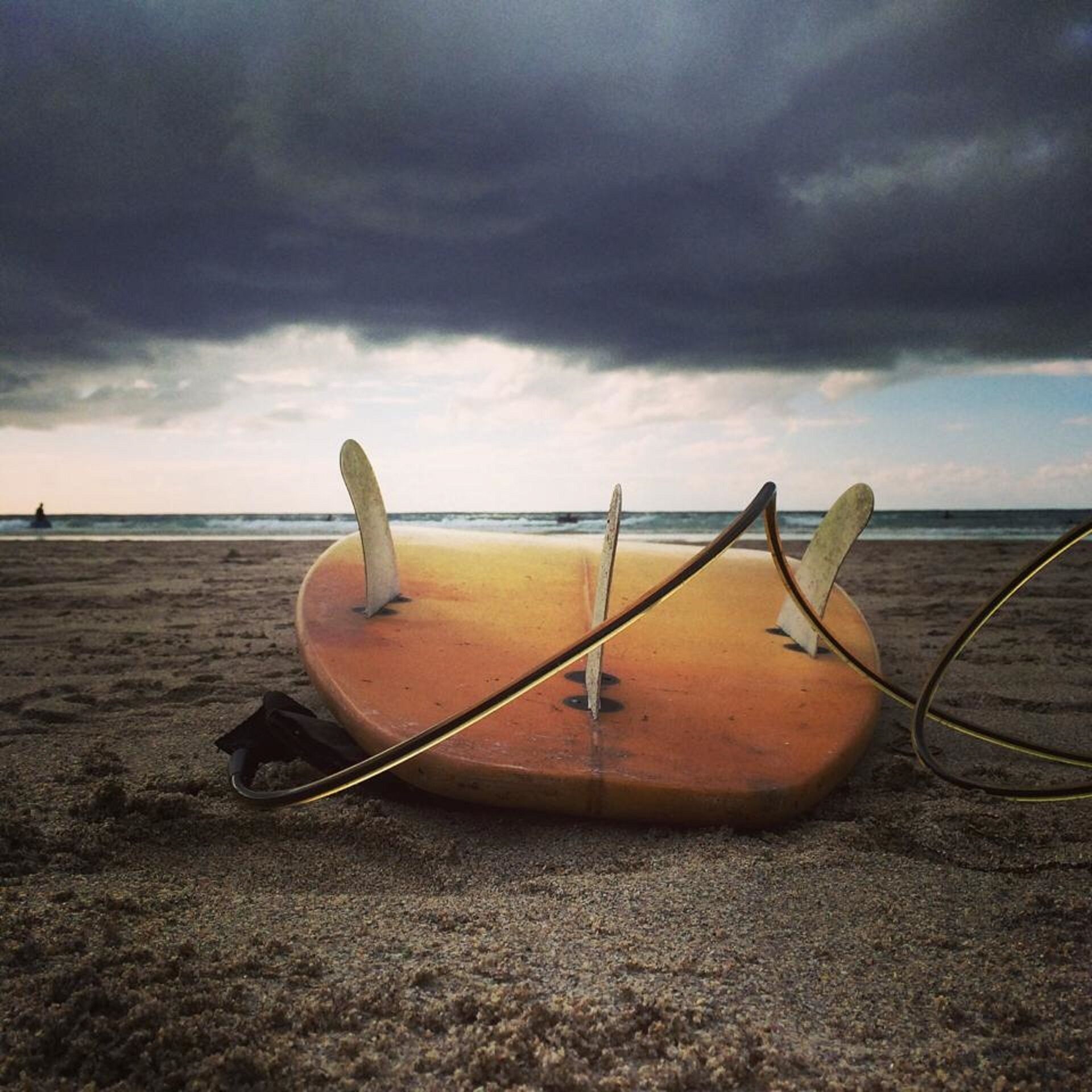 A surfboard on a sandy beach with a cloudy sky.