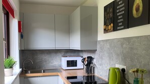 A compact kitchen with white cabinets, a microwave, a kettle, and a sink. There are two potted plants on the counter. - Holiday Cottage in Gulval Penzance Cornwall (Penzance Cornwall)