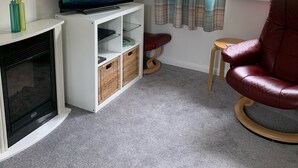 A living room with a fireplace, television, and a red leather chair. - Holiday Cottage in Gulval Penzance Cornwall (Penzance Cornwall)