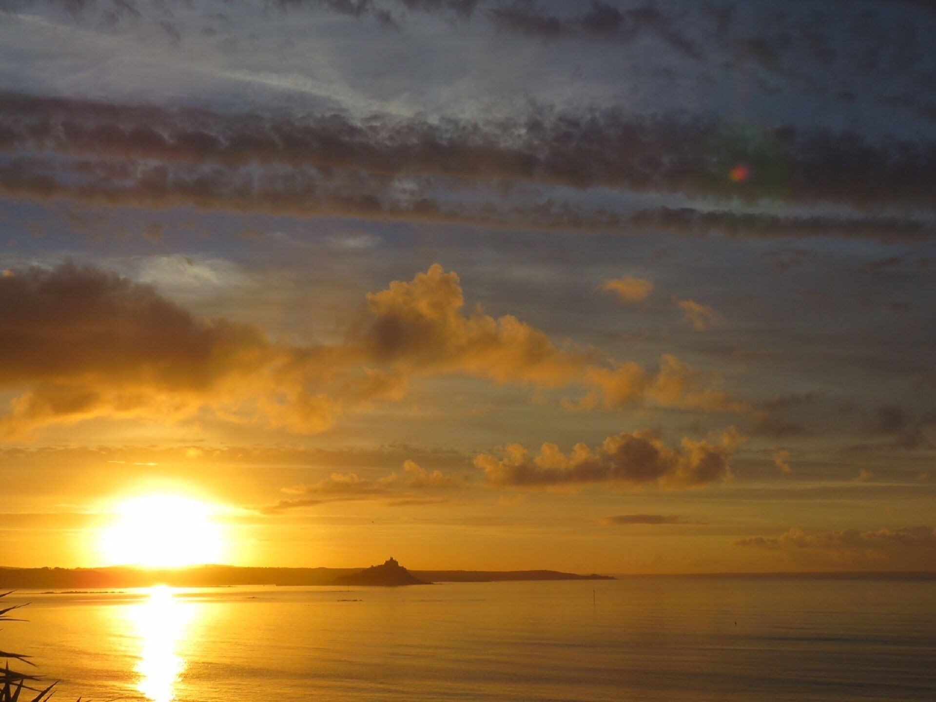 A sunset over a calm sea with a distant island silhouette.