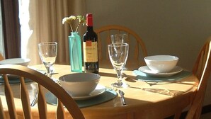 A dining table with a wine bottle, two wine glasses, a bowl, and a vase with flowers. - Holiday Cottage in Gulval Penzance Cornwall (Penzance Cornwall)