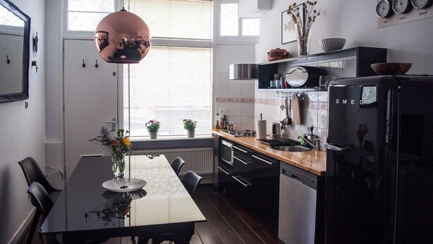 Une cuisine moderne avec une table à manger, des chaises, un luminaire suspendu et un réfrigérateur.