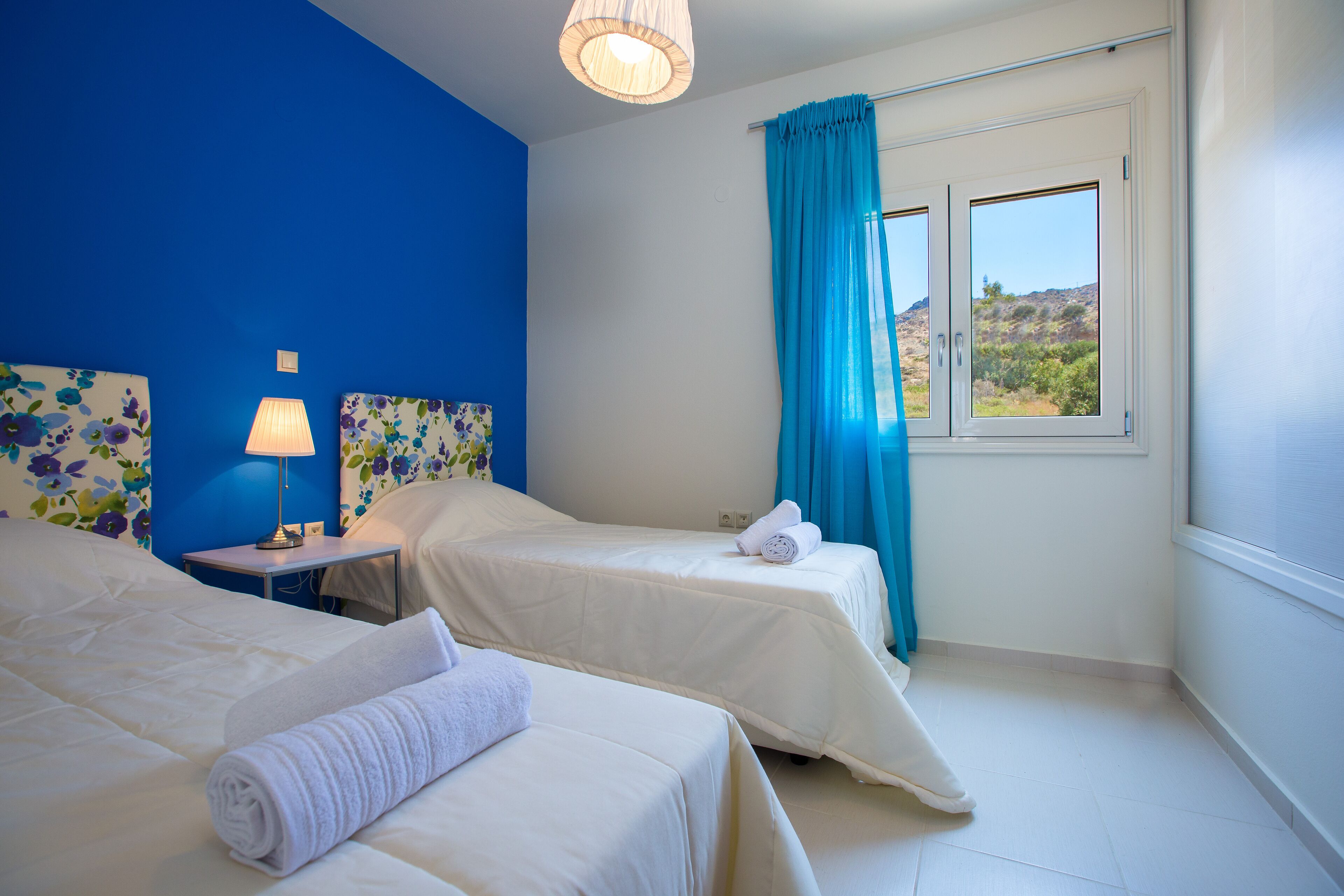 Une chambre d’hôtel avec deux lits, une table de chevet avec une lampe, une fenêtre avec des rideaux et une vue sur l’extérieur.
