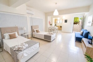 Une chambre d’hôtel avec deux lits, un canapé, une télévision, un bureau et un coin cuisine à l’arrière-plan.