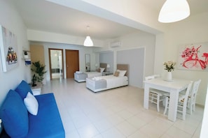 Una sala moderna con un sofá azul, una cama blanca y una mesa de comedor con sillas.
