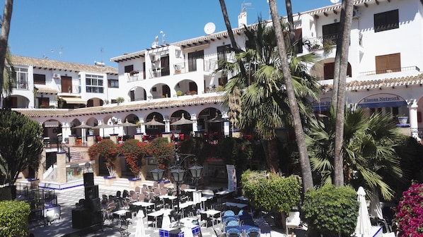 A courtyard with outdoor seating, palm trees, and a building with multiple balconies and arches.